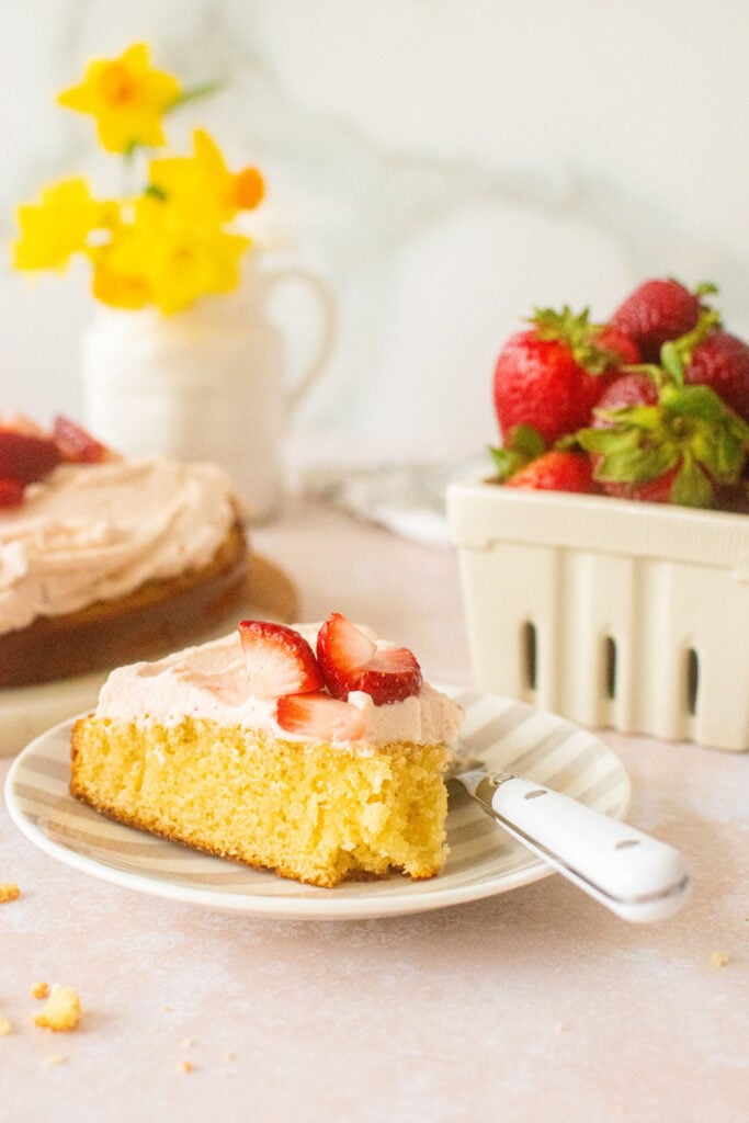 strawberry buttercream frosting on a vanilla cake slice with a bite taken out and a fork on plate.
