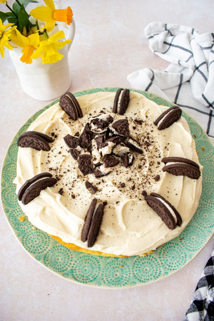 vanilla cake with cream cheese oreo frosting and oreos on top on a green plate.