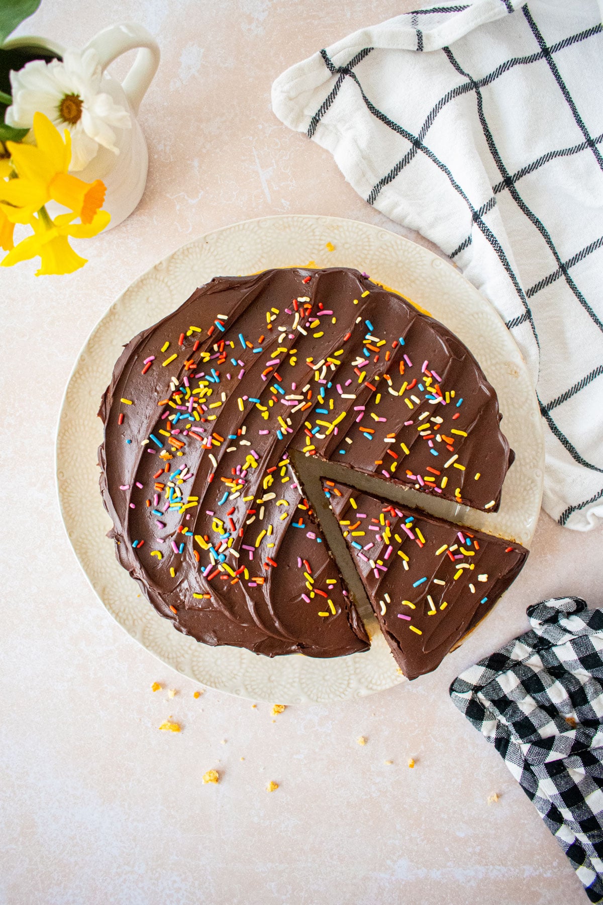 vanilla cake with chocolate ganache frosting and rainbow sprinkles on a white plate with a slice cut out.