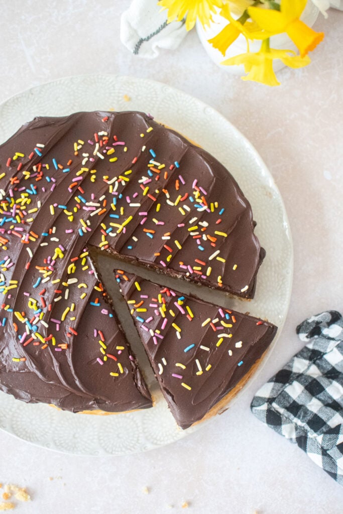 vanilla cake with chocolate ganache frosting and rainbow sprinkles with a slice cut out.