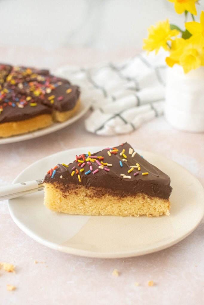 vanilla cake slice with chocolate ganache frosting and rainbow sprinkles on a plate with a fork.
