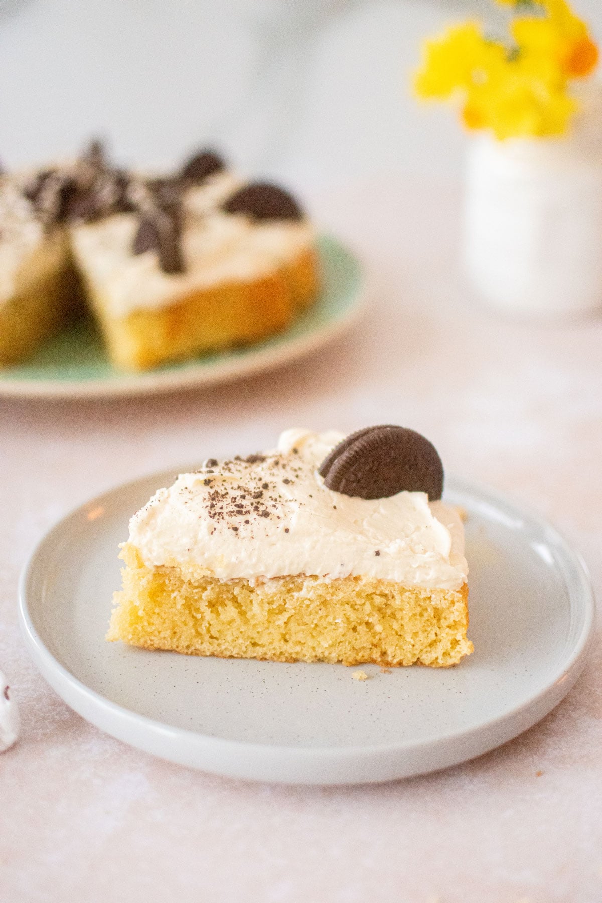 vanilla cake slice on a plate with oreo cookie on top.