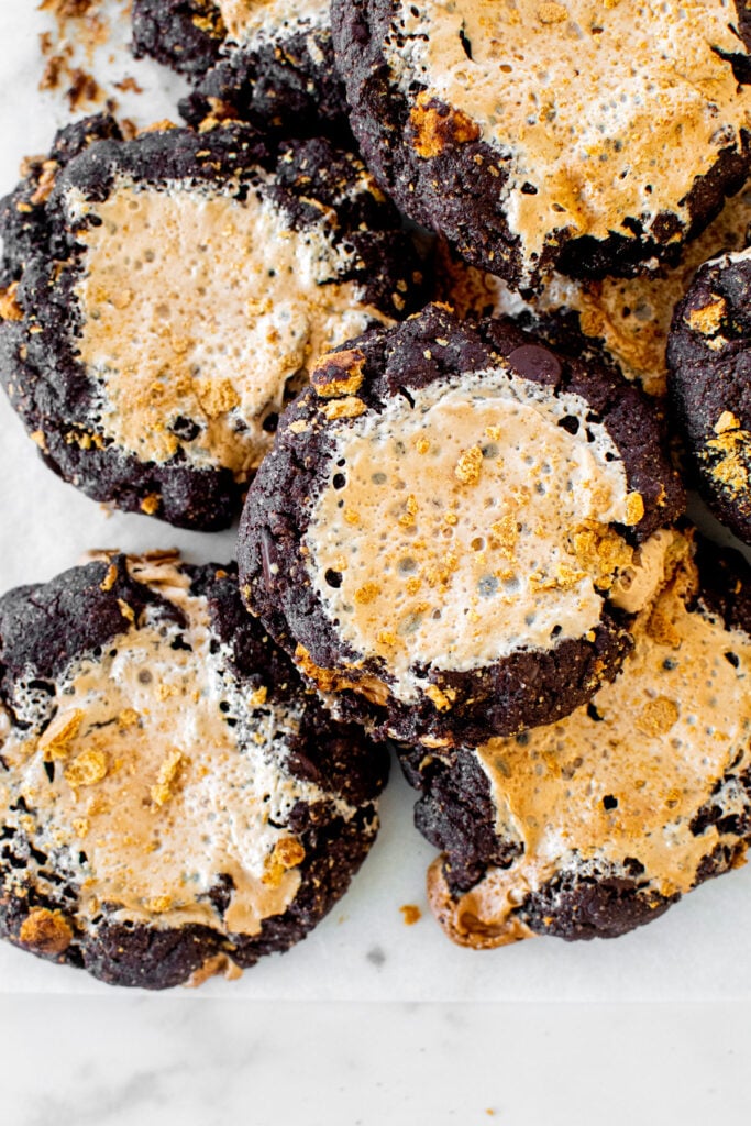 bakery style chocolate smores cookies with fluff on white parchment paper on a marble countertop.