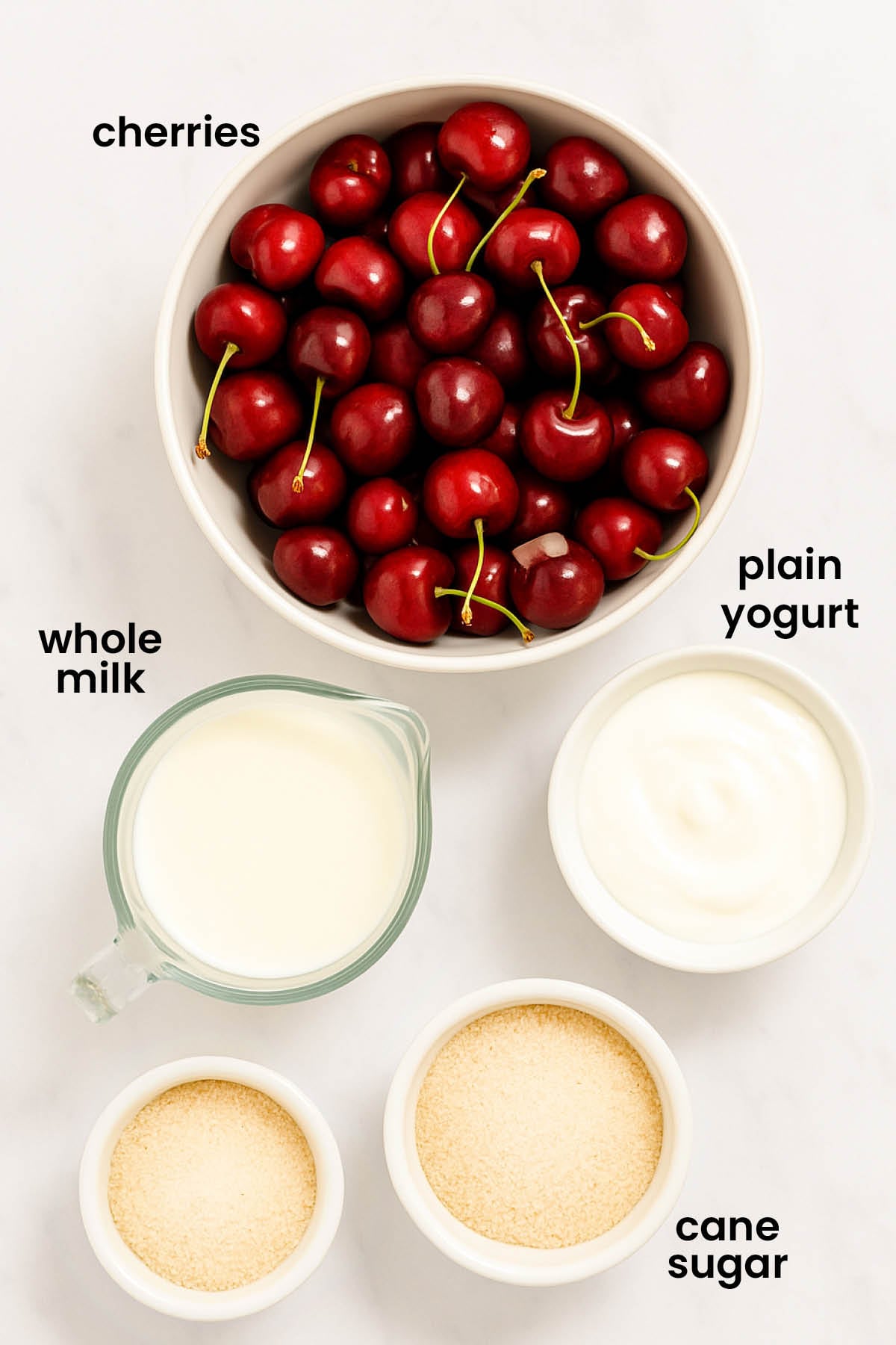 individual ingredients for healthy homemade cherry frozen yogurt laid out against a white background.