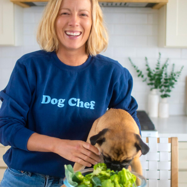 dog chef sweatshirt on a woman in the kitchen with her pug at the counter.