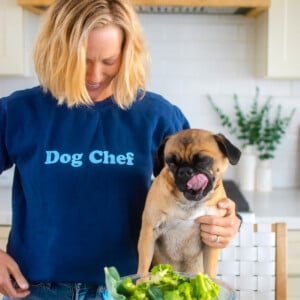 dog chef sweatshirt on a woman in the kitchen with her pug at the counter.