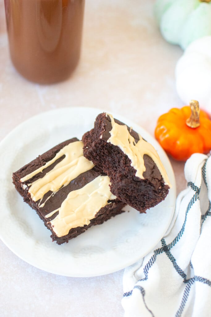 two pumpkin spice latte brownies on a white plate, one with a bite taken out with a glass of chocolate milk.