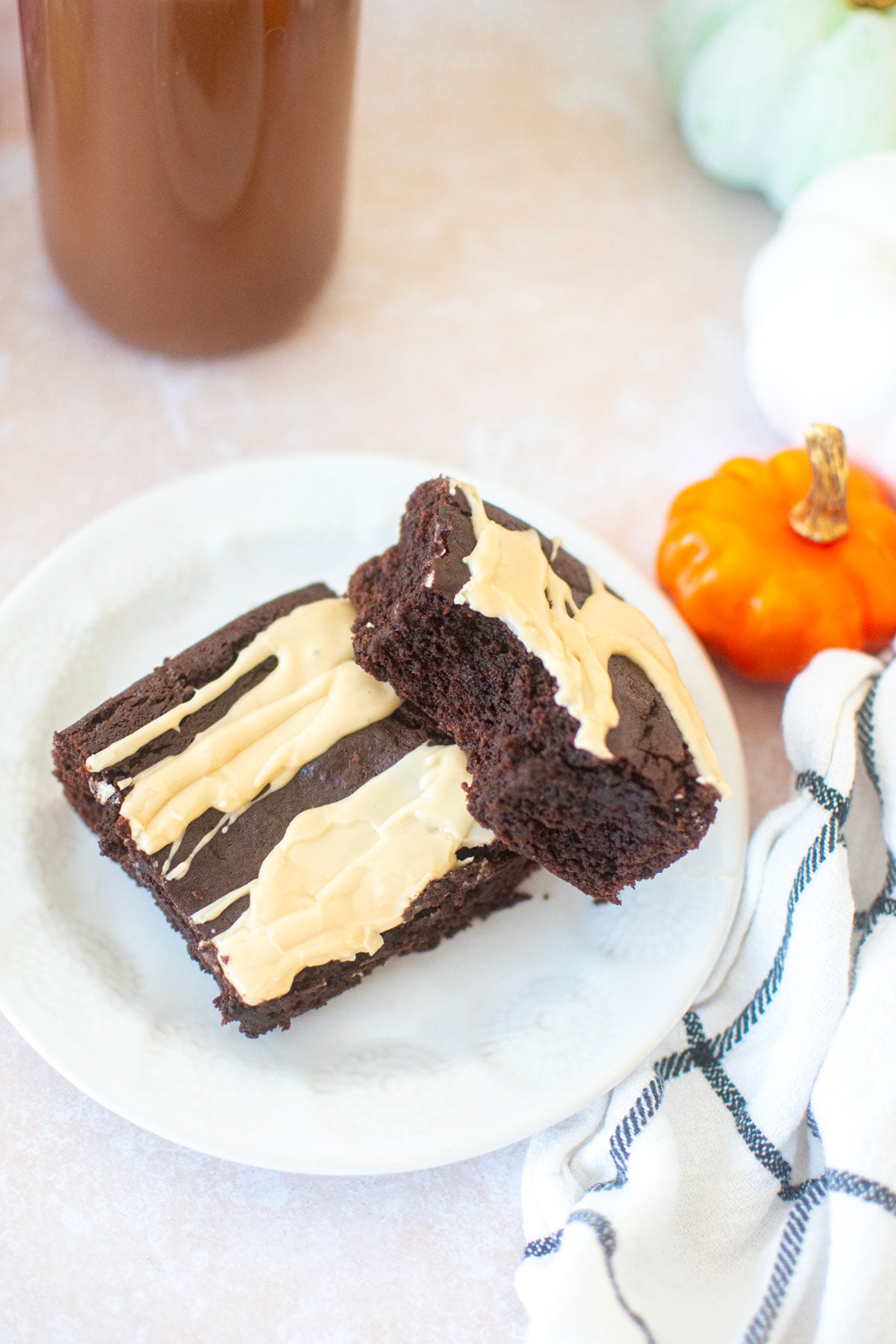 two pumpkin spice latte brownies on a white plate, one with a bite taken out with a glass of chocolate milk.
