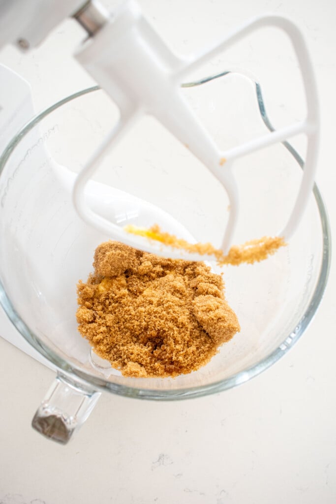 butter and brown sugar in a glass mixing bowl on a marble counter.
