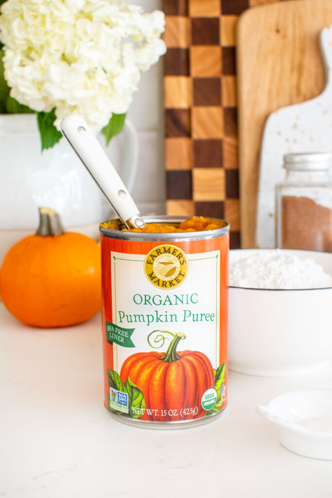 can of pumpkin open on kitchen counter with a spoon in it with a pumpkin and bowl of powdered sugar.