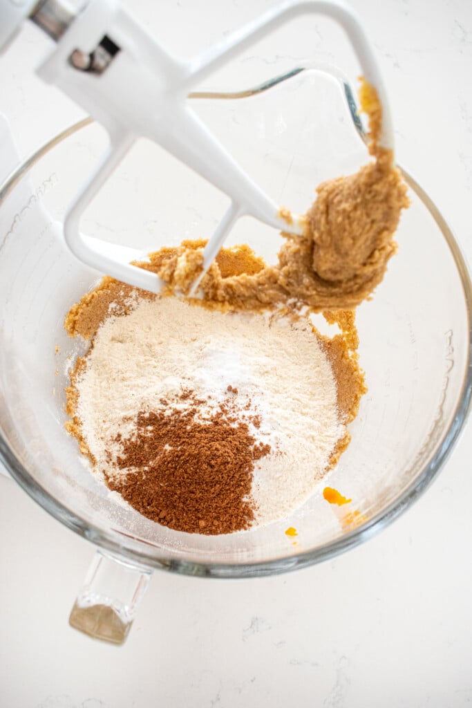 ingredients for pumpkin spice cookies in a glass mixing bowl on a marble counter.