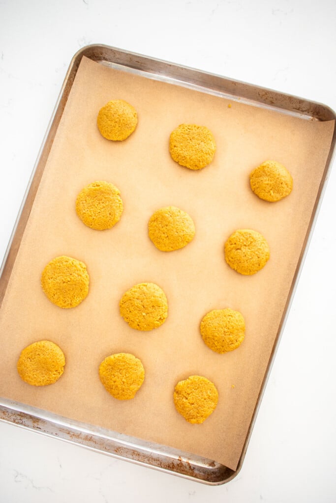 pumpkin spice cookie dough balls on a parchment paper lined baking sheet on a marble counter.