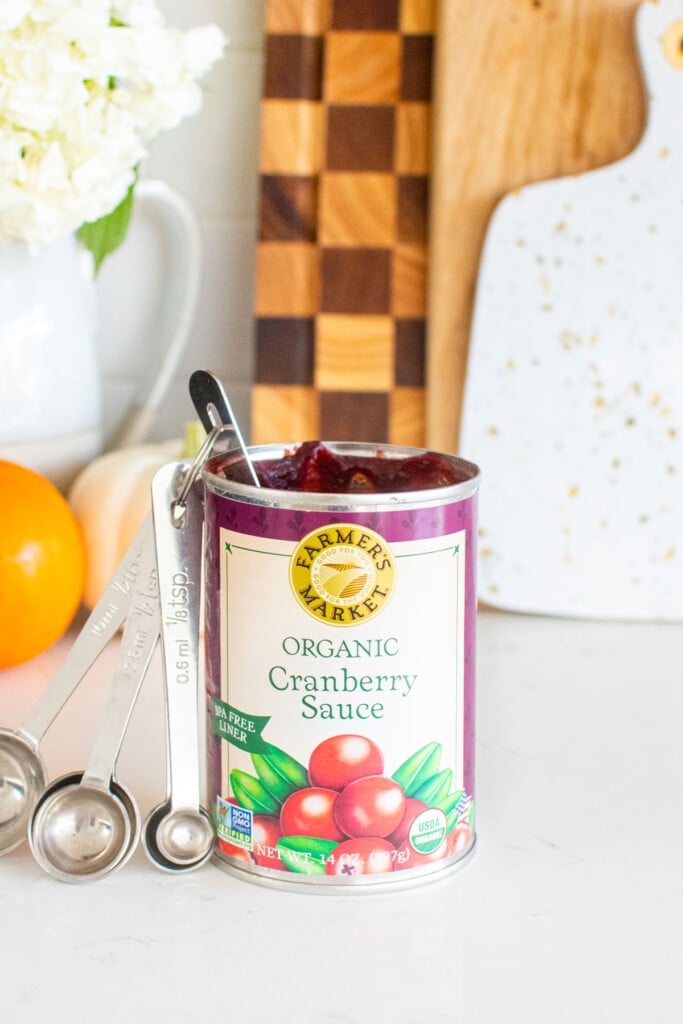 open jar of cranberry sauce on a kitchen counter with measuring spoons in it and pumpkins.