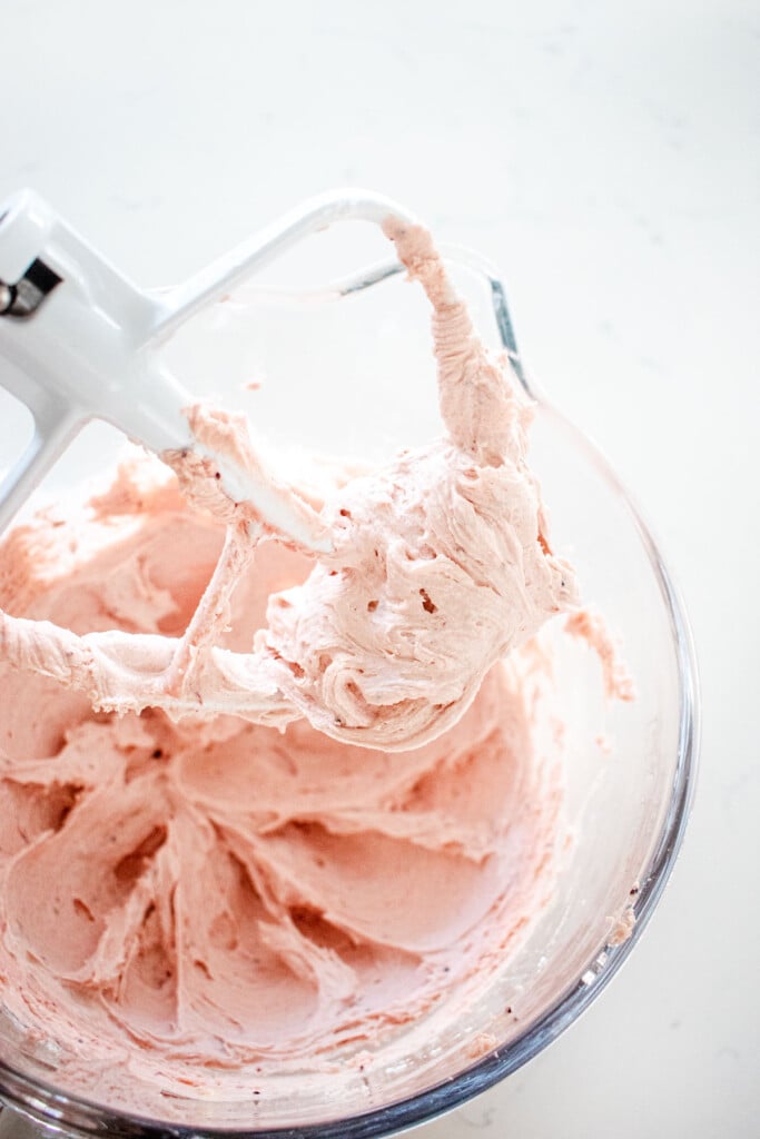 cranberry buttercream filling in a glass mixing bowl on a marble counter.