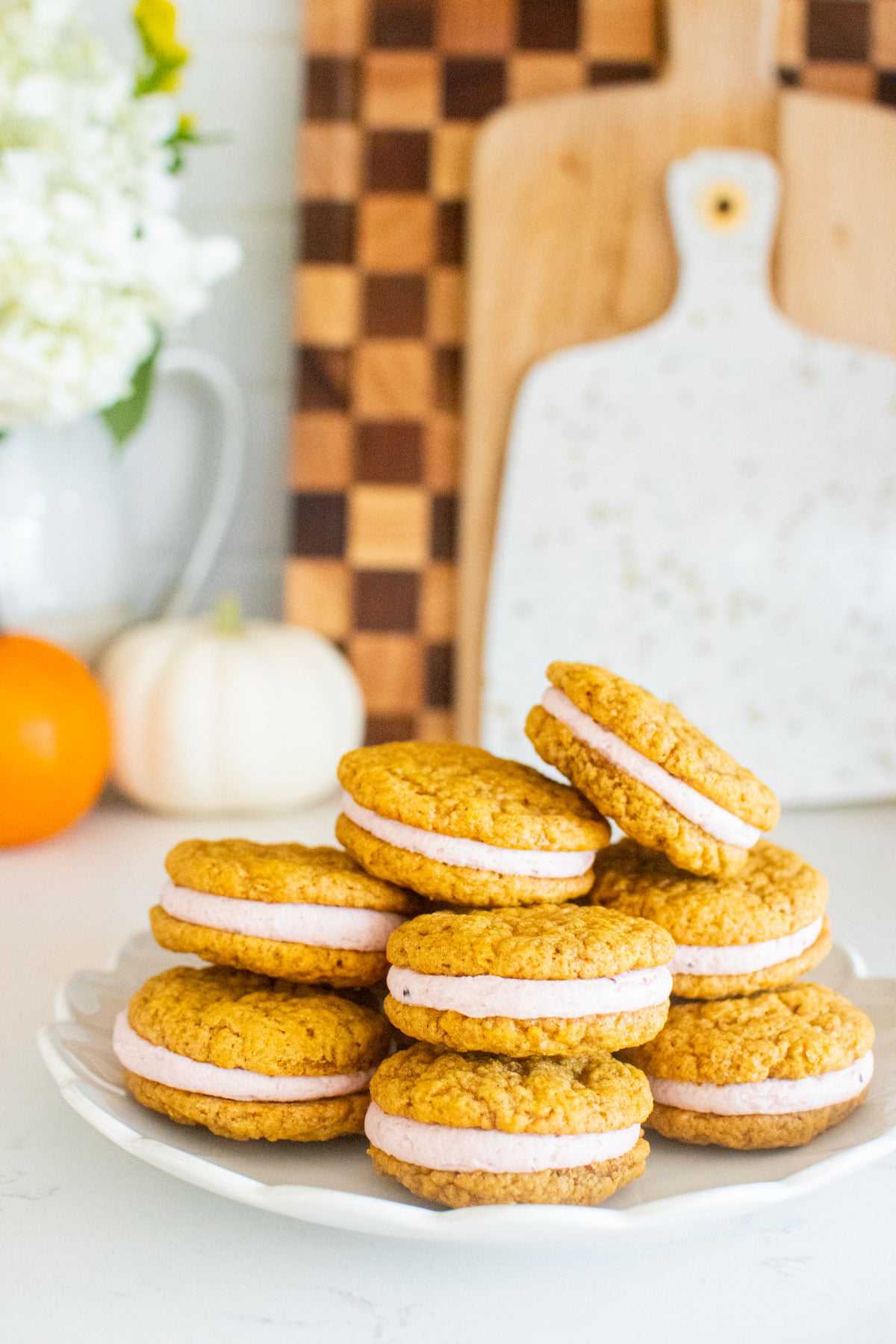 plate of pumpkin spice cranberry sandwich cookies on a white marble counter with pumpkins.