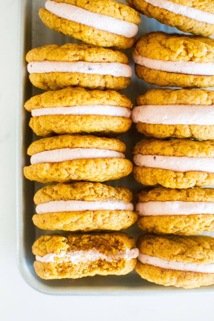 pumpkin spice cranberry sandwich cookies on a baking sheet on a marble counter.