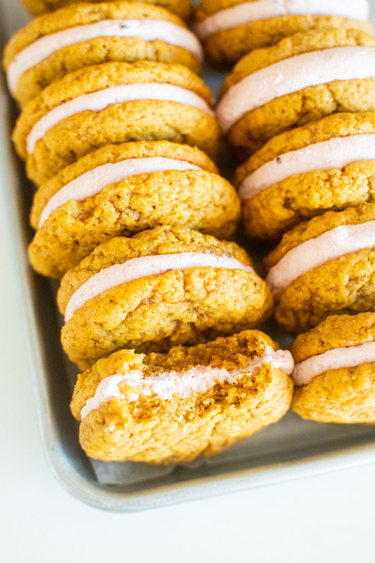 pumpkin spice cranberry sandwich cookies on a baking sheet on a marble counter.
