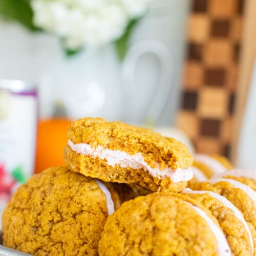 pumpkin spice cranberry sandwich cookies on a baking sheet on a marble counter with pumpkins.