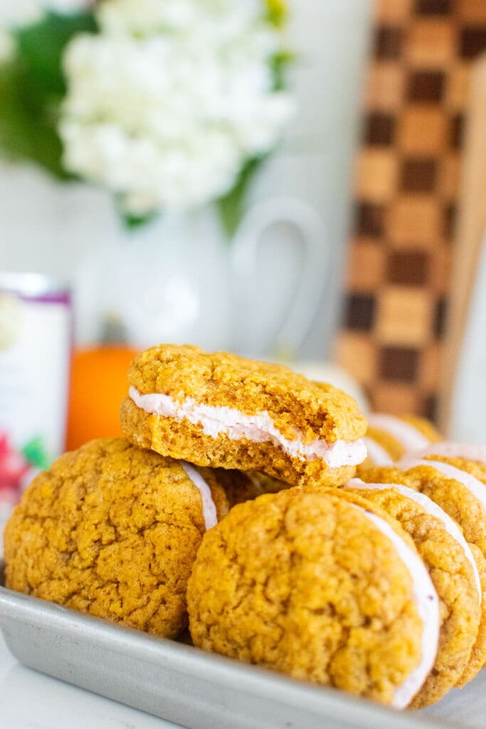 pumpkin spice cranberry sandwich cookies on a baking sheet on a marble counter with pumpkins.