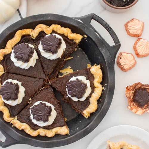 chocolate pumpkin pie without eggs with whipped cream dollops and chocolate leaves on top cut into slices on a marble table.