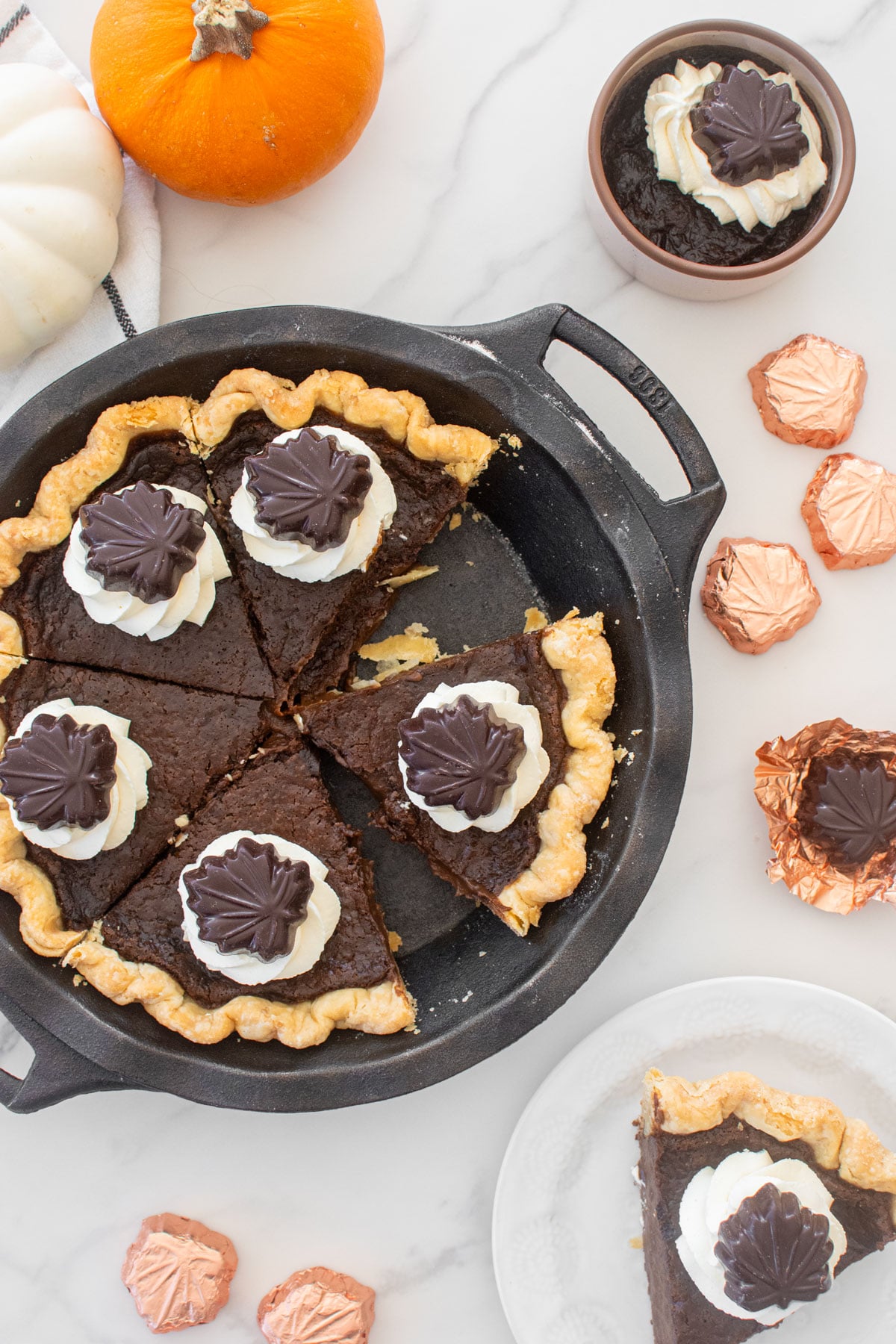 chocolate pumpkin pie without eggs with whipped cream dollops and chocolate leaves on top cut into slices on a marble table.