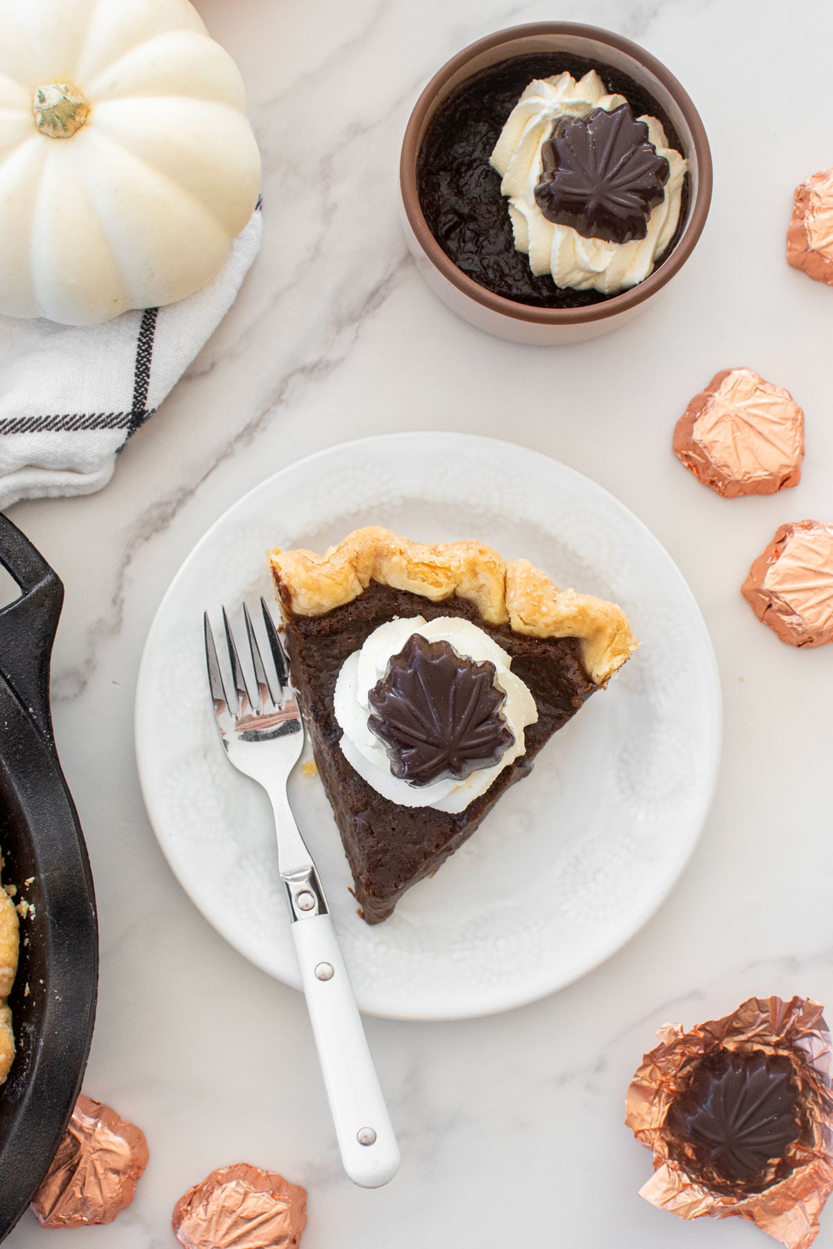 slice of chocolate pumpkin pie without eggs with a dollop of whipped cream and chocolate leaf on top on a plate on a marble counter.