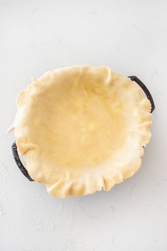 pie crust in a cast iron pie pan on a white marble counter.