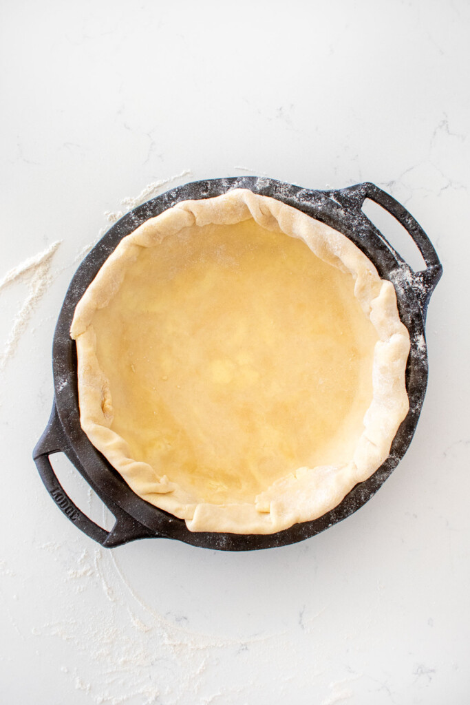 pie crust in a cast iron pie pan on a white marble counter.