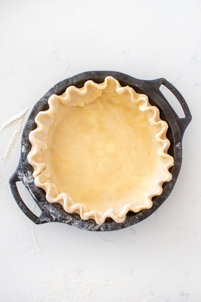 fluted pie crust in a cast iron pie pan on a white marble counter.