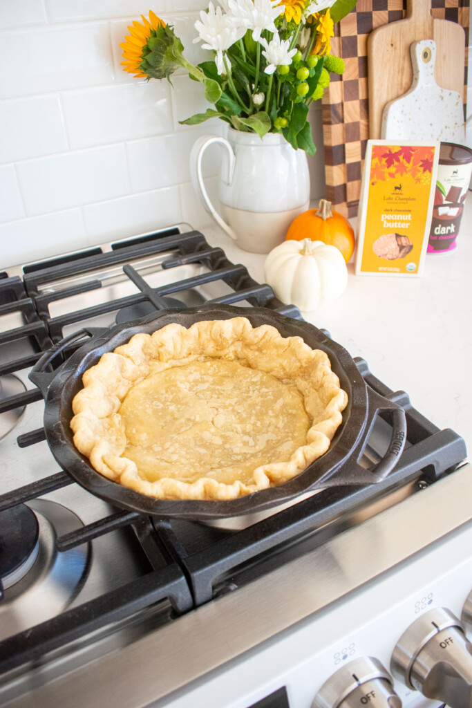 partially baked pie crust in a cast iron pie pan on a stovetop.