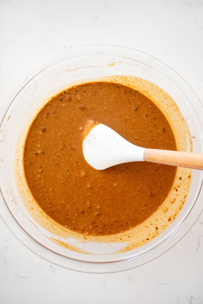 chocolate pumpkin pie filing in a glass mixing bowl with a spatula on a white marble counter.
