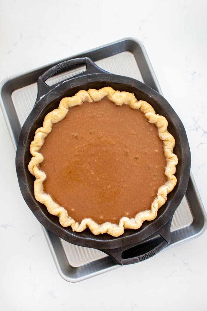 chocolate pumpkin pie filling in a partially baked pie crust on a baking sheet on a white marble counter.