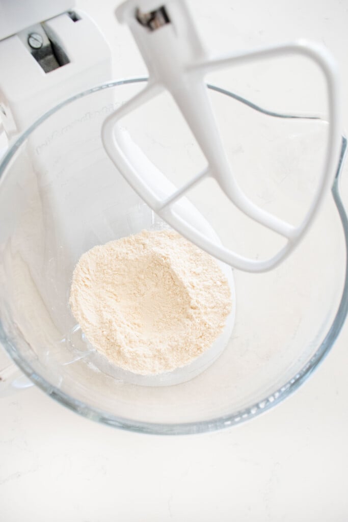 flour in a glass mixing bowl on a white marble counter.