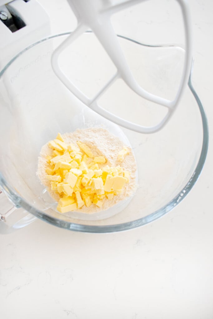 ingredients for pie dough in a glass mixing bowl on a white marble counter.