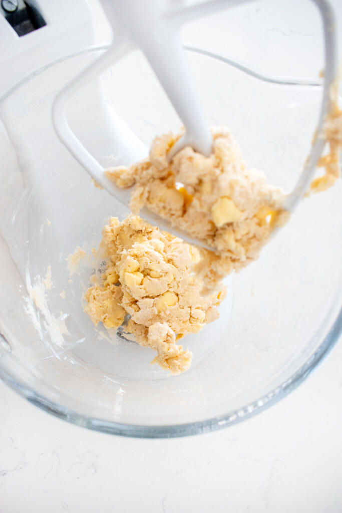 pie dough in a glass mixing bowl on a white marble counter.