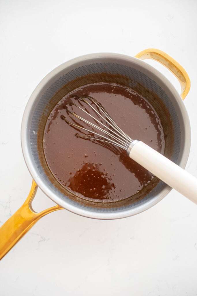 gingerbread caramel sauce with a whisk in a titanium pot on a white marble counter.