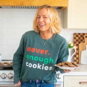 woman wearing a garment dyed sweatshirt with never enough cookies text on it holding a plate of cookies in the kitchen.