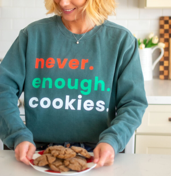 woman wearing a garment dyed sweatshirt with never enough cookies text on it holding a plate of cookies in the kitchen.