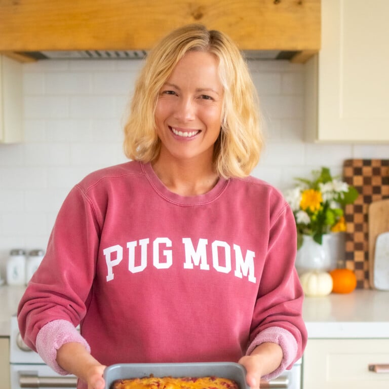woman in kitchen wearing a red sweatshirt with pug mom in text on it.