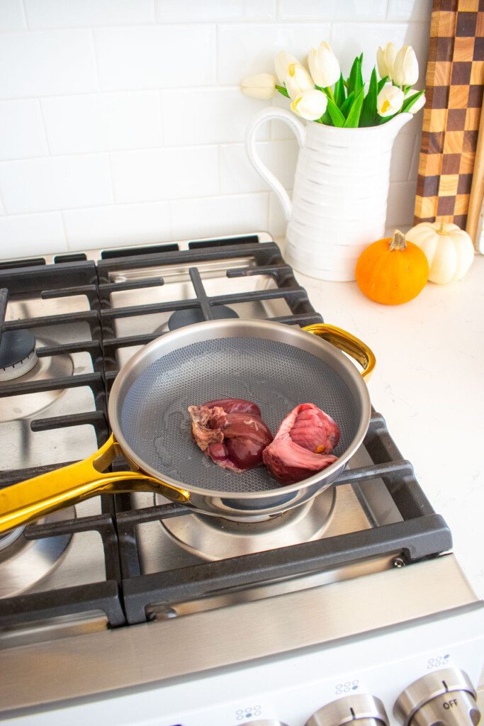 raw turkey giblets in a skillet on the stovetop.