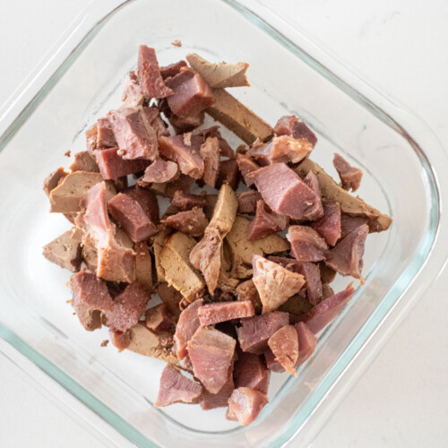 chopped turkey giblets in a glass tupperware on a white marble counter.