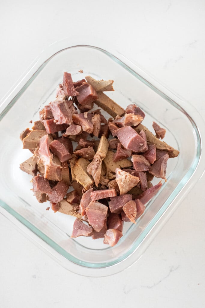chopped turkey giblets in a glass tupperware on a white marble counter.