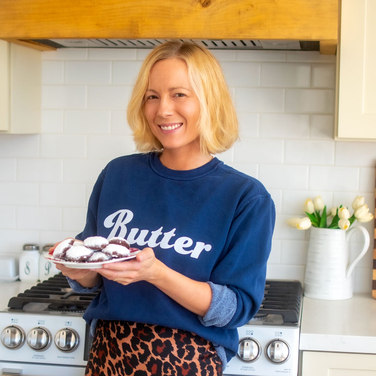 woman wearing a butter sweatshirt holding a plate of cookies in the kitchen.