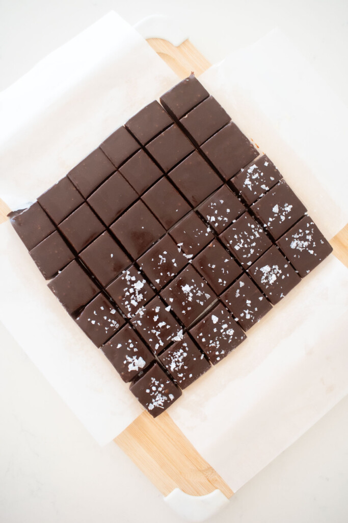 homemade chewy chocolate caramel candy cut into squares on a wood cutting board on a marble counter.