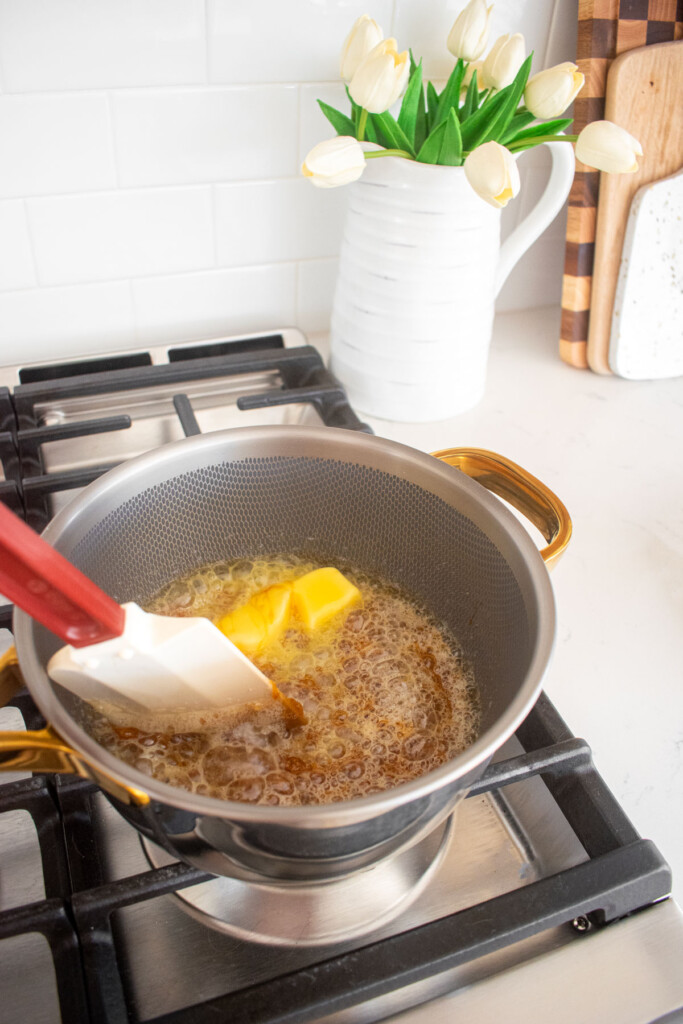 butter being added to melted cane sugar in a pot on the stovetop.
