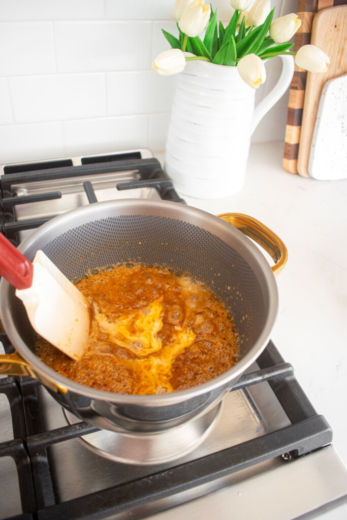 cream being added to caramel in a pot on the stovetop.