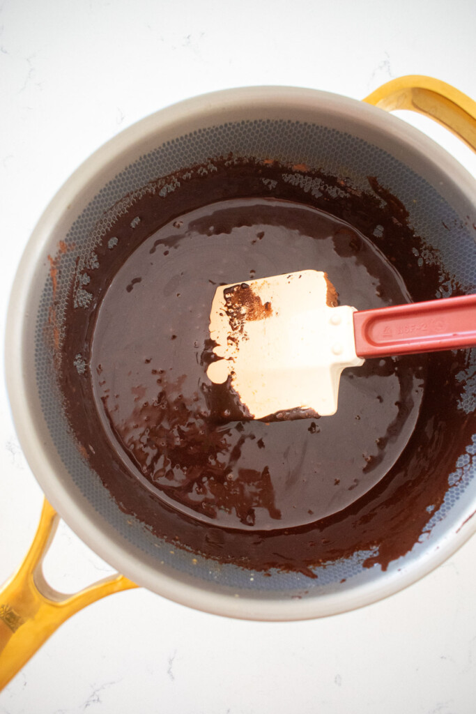 homemade chewy chocolate caramel candy in a pot with a spatula on a white marble counter.