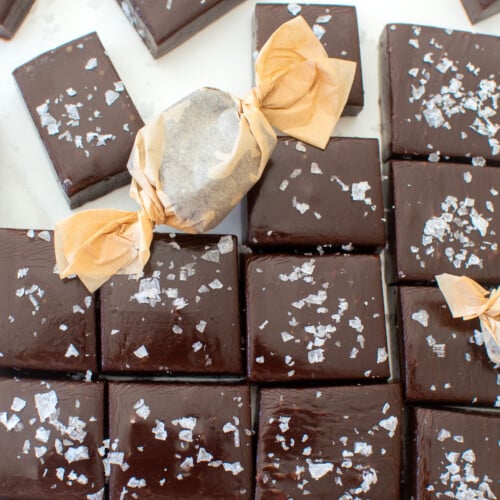 homemade chewy chocolate caramel candy with flaky sea salt cut into squares on a white marble counter.