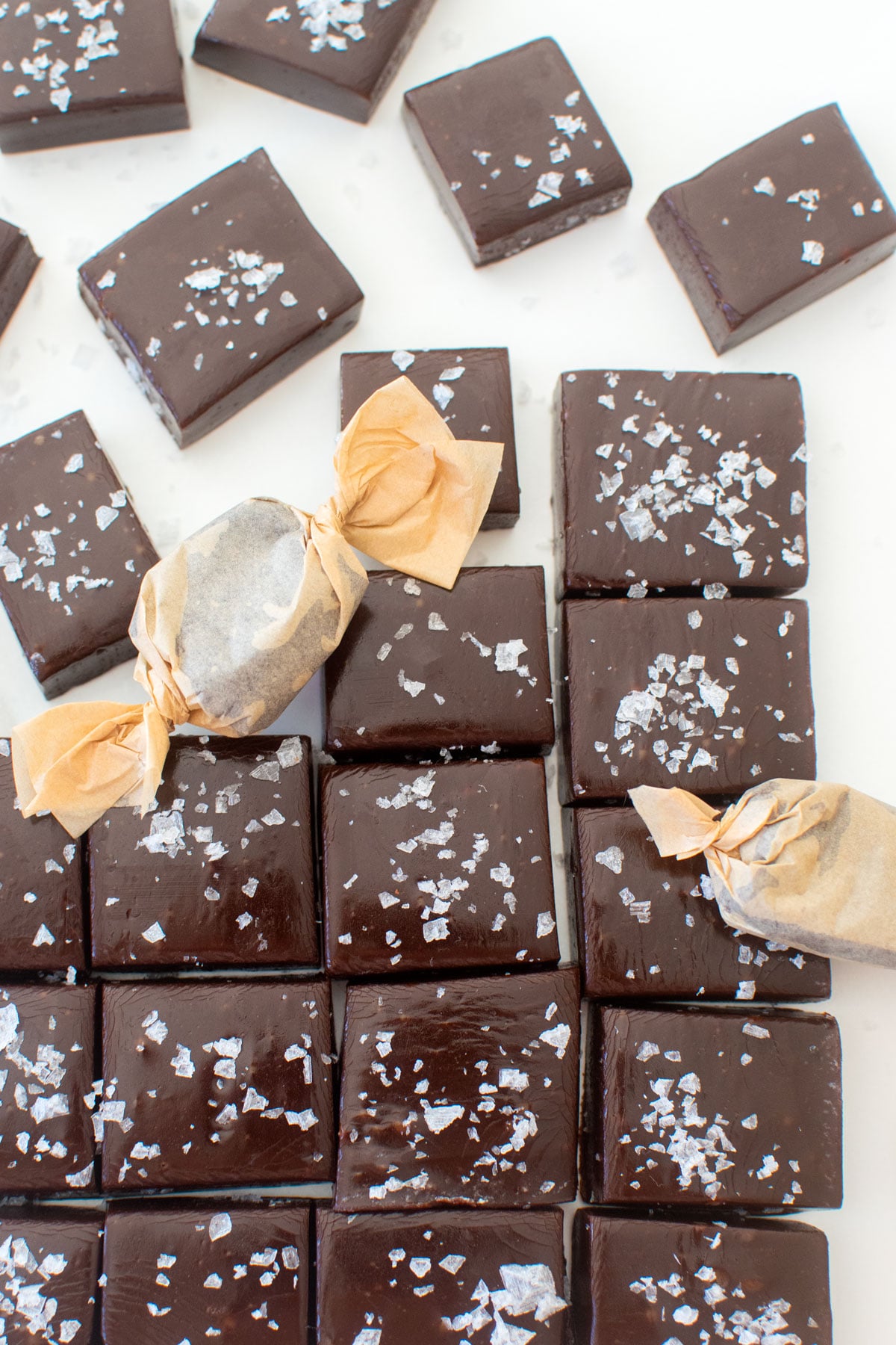 homemade chewy chocolate caramel candy with flaky sea salt cut into squares on a white marble counter.