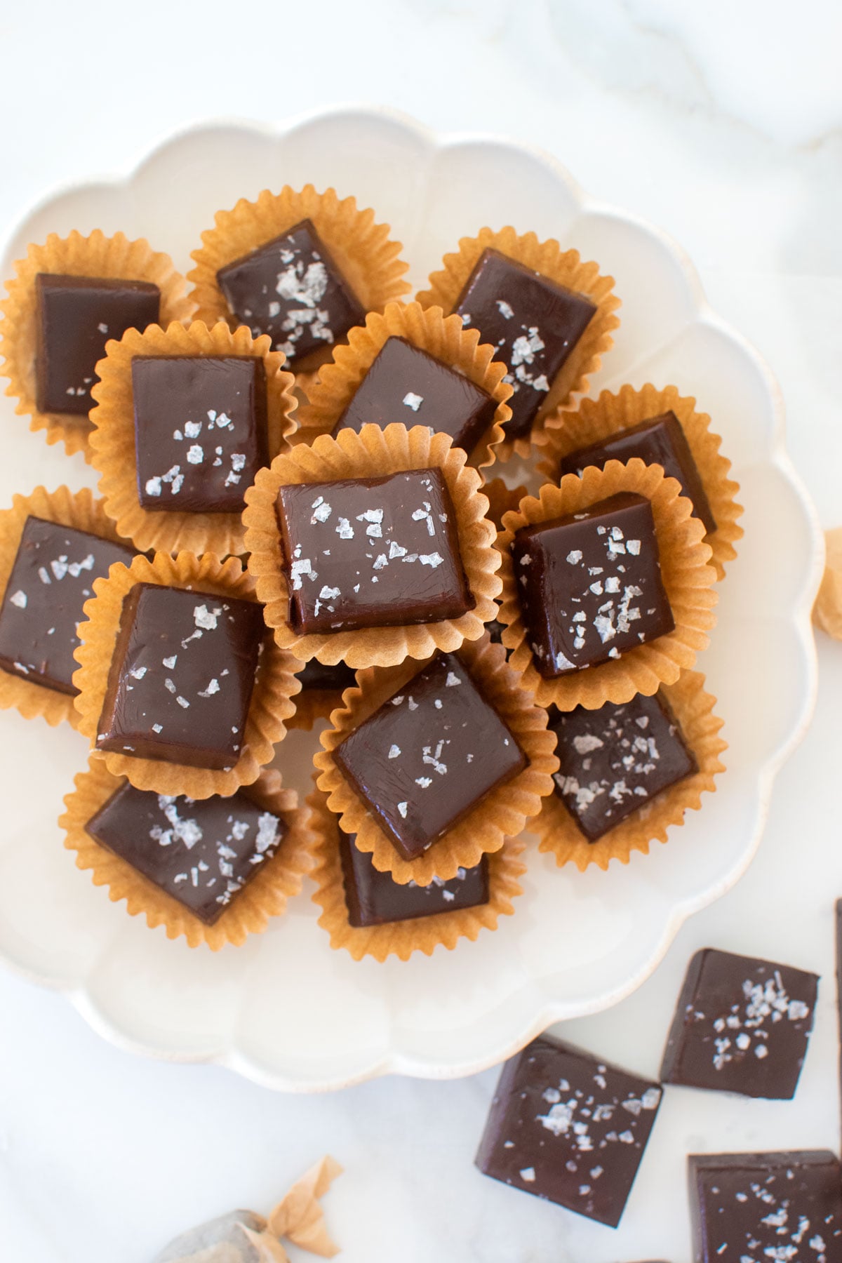 homemade chewy chocolate caramel candy with flaky sea salt in candy cups on a white plate.